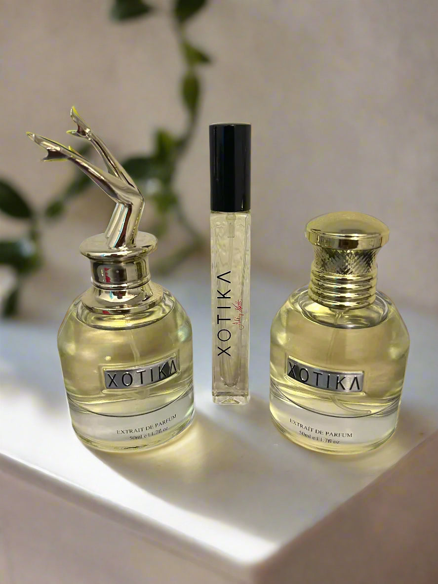 Three Xotika perfume bottles on a reflective surface with a gradient purple background